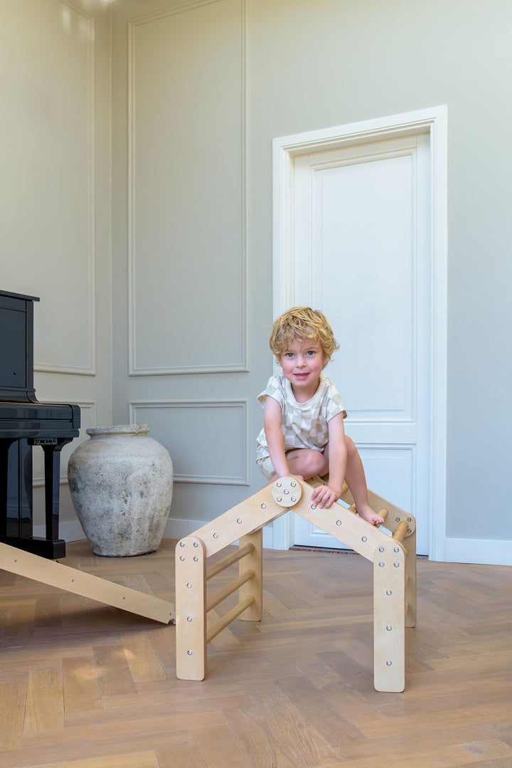A young boy climbs to the top of the Babiem Ben Climbing House, smiling as he plays on the natural wooden indoor play equipment.