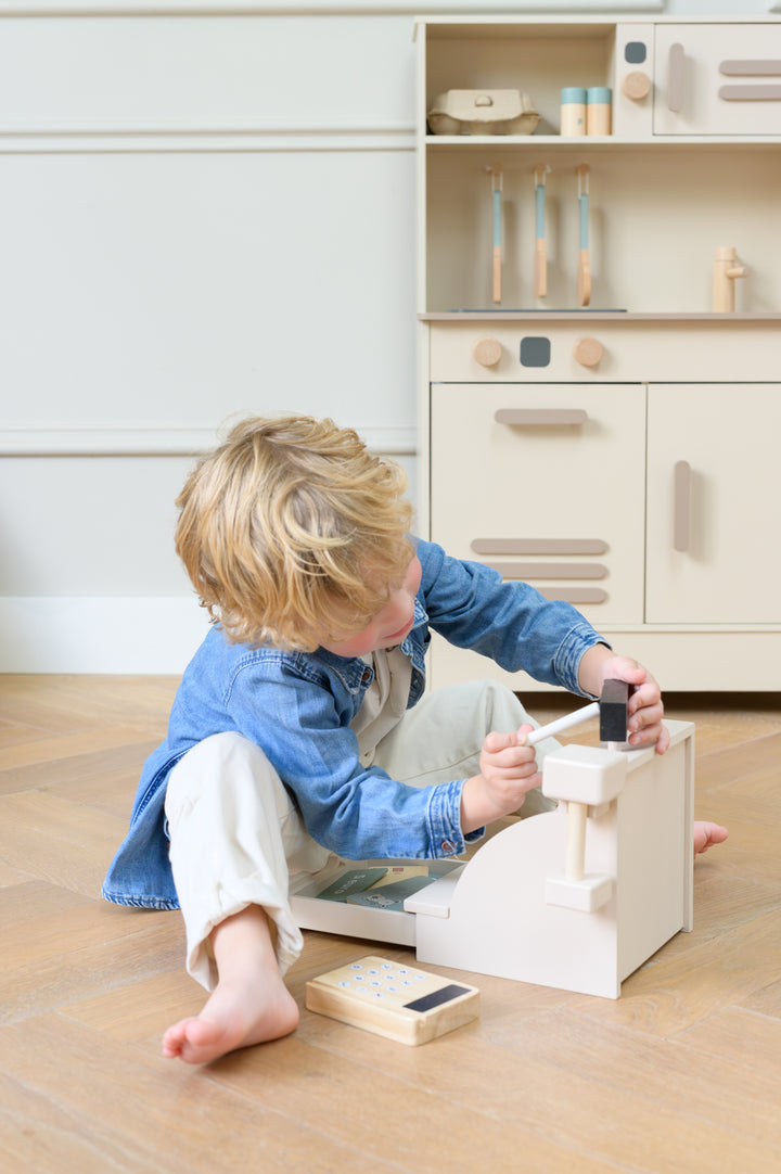 Child playing with the Babiem Cash Register Coco while seated on the floor near Babiem play kitchen Noor
