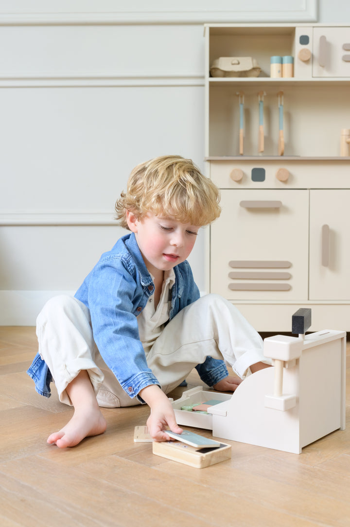 Child playing with the Babiem Cash Register Coco on the floor near a toy kitchen.
