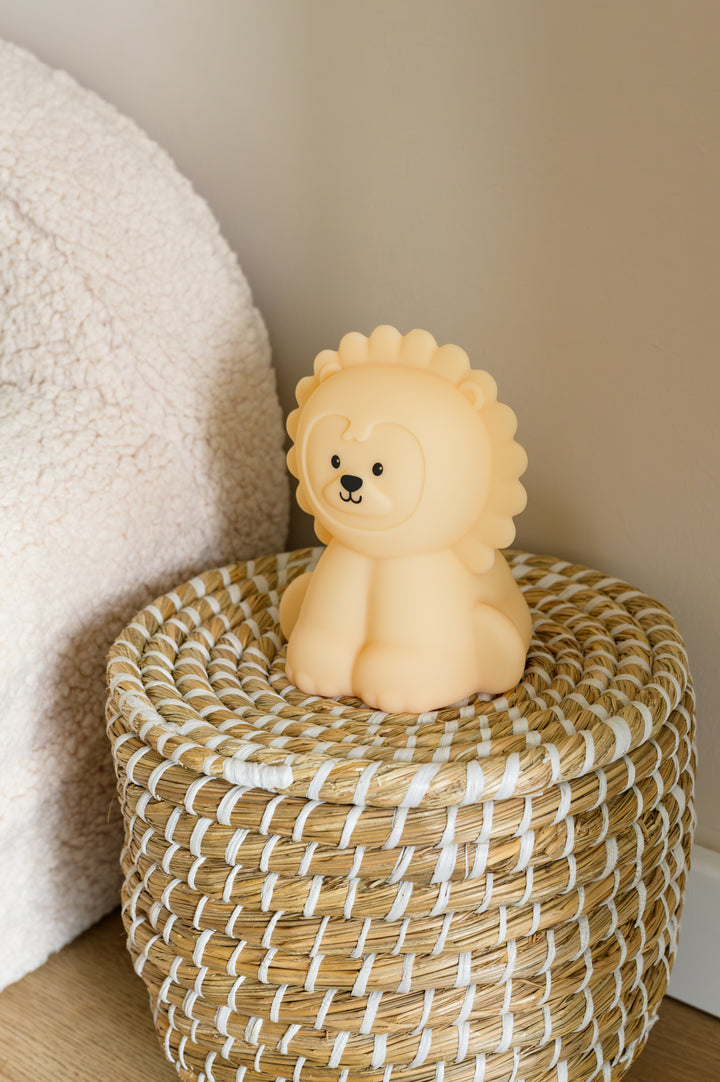 A cute lion night light named Babiem Lucas, placed on a woven basket in natural daylight for a playful and safe nursery vibe.