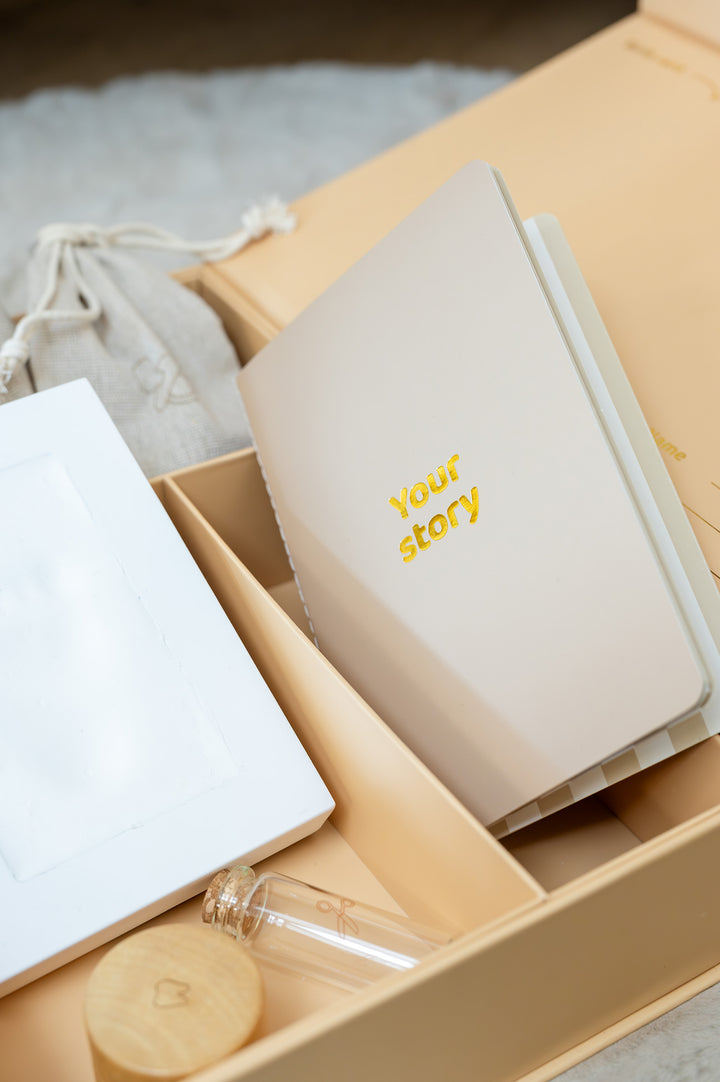 Babiem memory box featuring a booklet titled "Your story", a glass vial with wooden lid for the first lock of hair, a linen pouch for the first pacifier, and a white frame, a beautiful way to preserve your baby’s earliest memories.