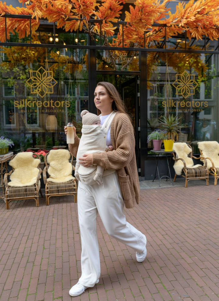 A parent walking outside with their baby in the Babiem baby carrier Chloé, enjoying a calm city moment. The neutral-toned carrier and soft knitwear reflect Babiem’s warm and natural style, combining comfort, safety and everyday elegance.