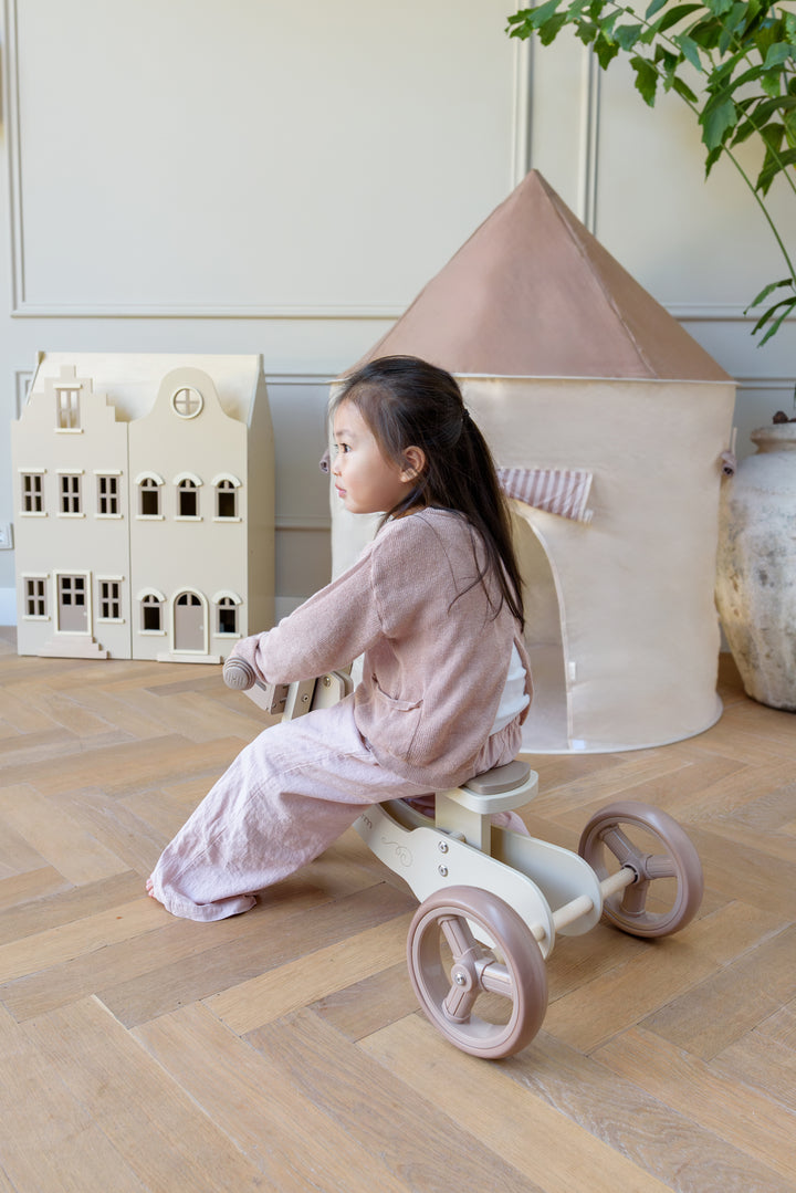 A child sitting on the Babiem balance bike James indoors, shown here in its three-wheel setup, which can be easily converted from a two-wheeler to a stable three-wheeler.