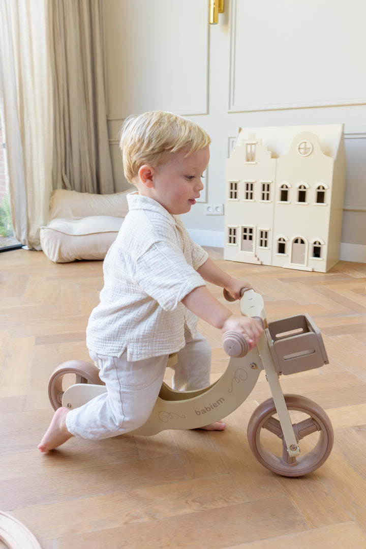 A young child riding the Babiem balance bike James indoors, holding the handlebars while moving across the wooden floor.