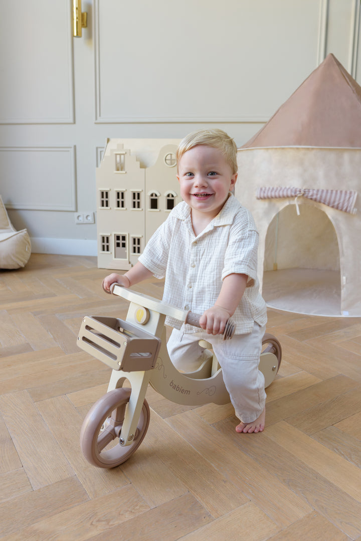 A young child riding the Babiem balance bike James indoors, holding the handlebars while smiling