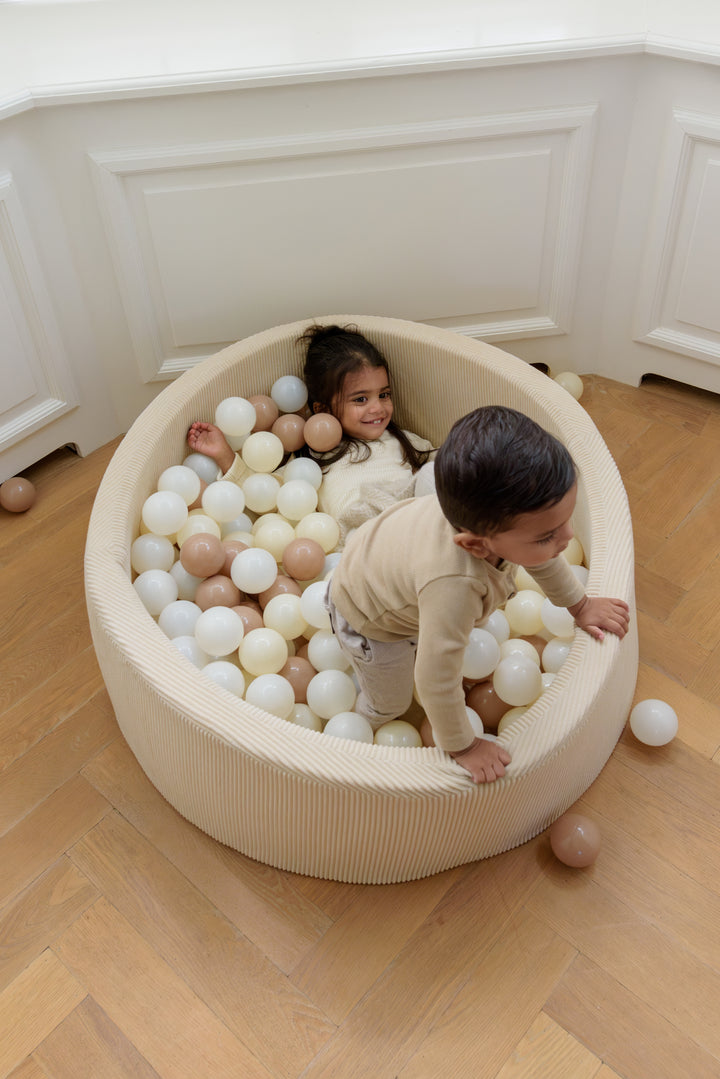 Two children playing inside the Babiem ball pit Milou, filled with soft pastel-colored balls, smiling and having fun in a cozy indoor setting.