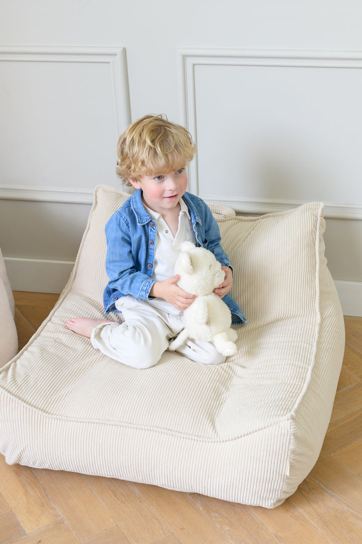 Child sitting on the Babiem beanbag Bruno in a soft beige fabric holding a stuffed animal and smiling in a bright room