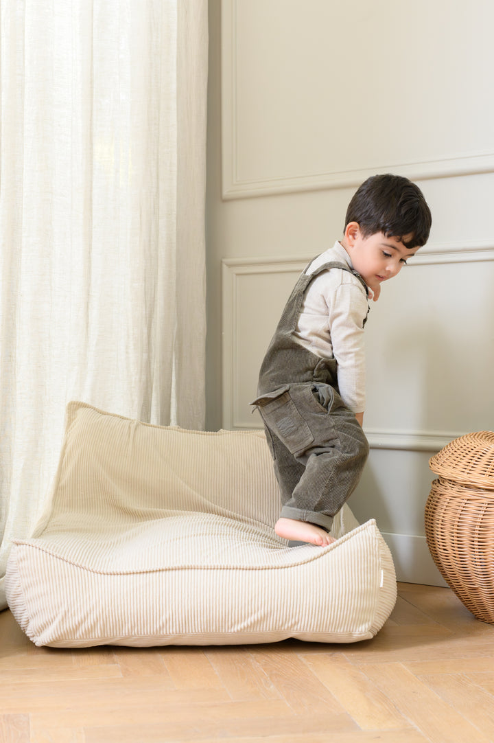 A child climbing onto the soft, corduroy-textured Babiem beanbag Bruno in a light and cozy room with floor-to-ceiling curtains.