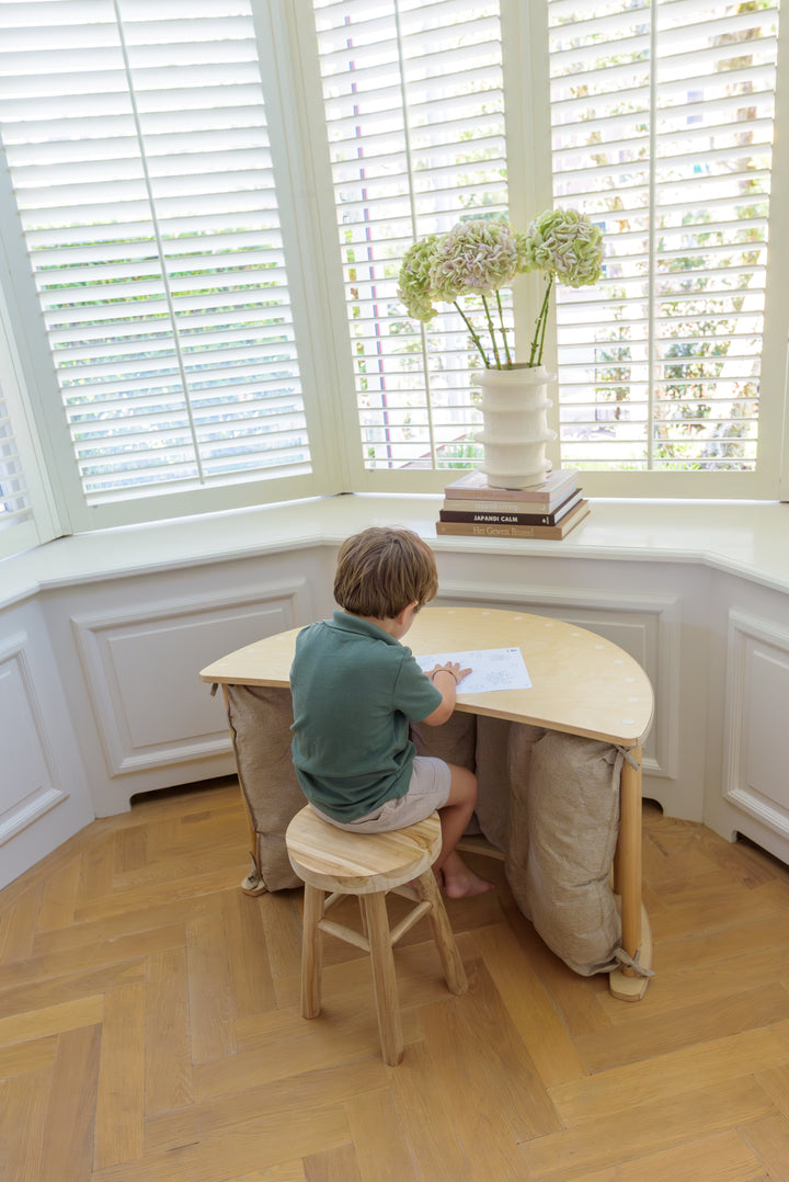 A young child sits at the Babiem climbing arch Ben transformed into a desk, drawing on paper in a bright room with natural light and a cozy setup.