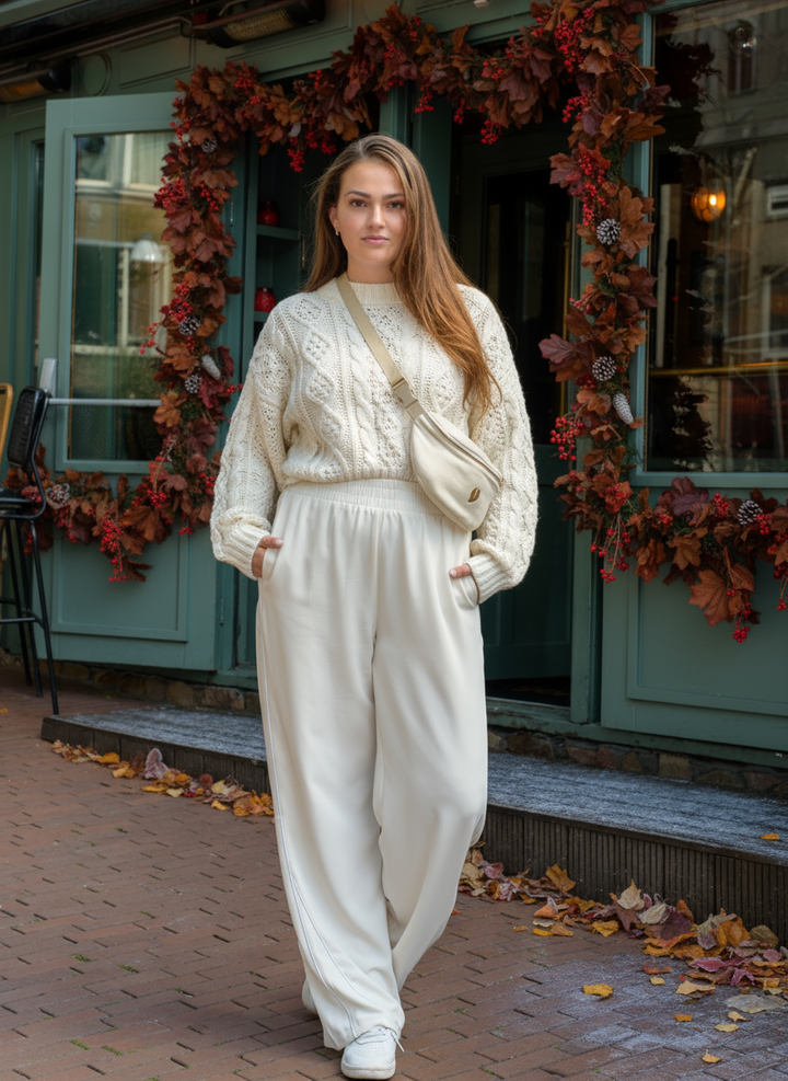 A woman standing outside a café wearing the Babiem fanny pack in a soft neutral tone. The cozy knit sweater and calm autumn setting reflect Babiem’s warm and natural aesthetic.