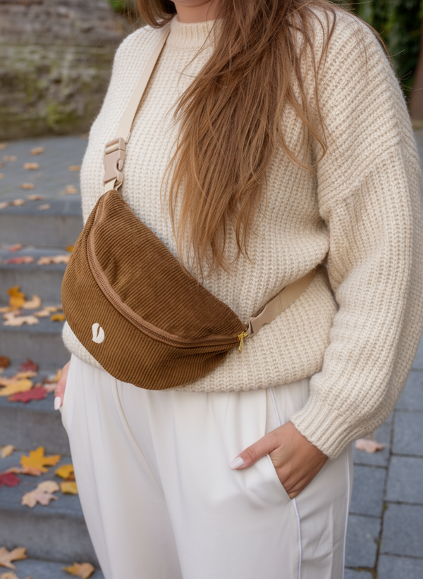 A close-up of a woman wearing the Babiem fanny pack from the baby carrier Luca. The soft brown corduroy fabric and neutral tones create a warm, natural look that blends comfort and style.