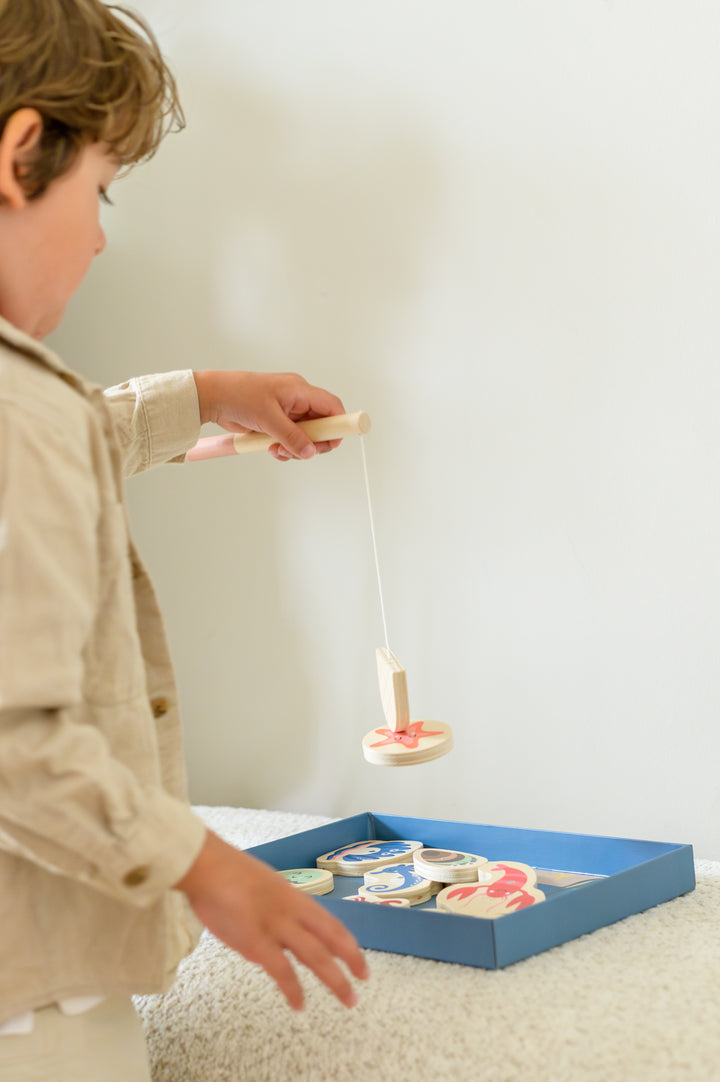 Young child holding a wooden sea animal with magnetic fishing rod from Babiem fishing game Emma