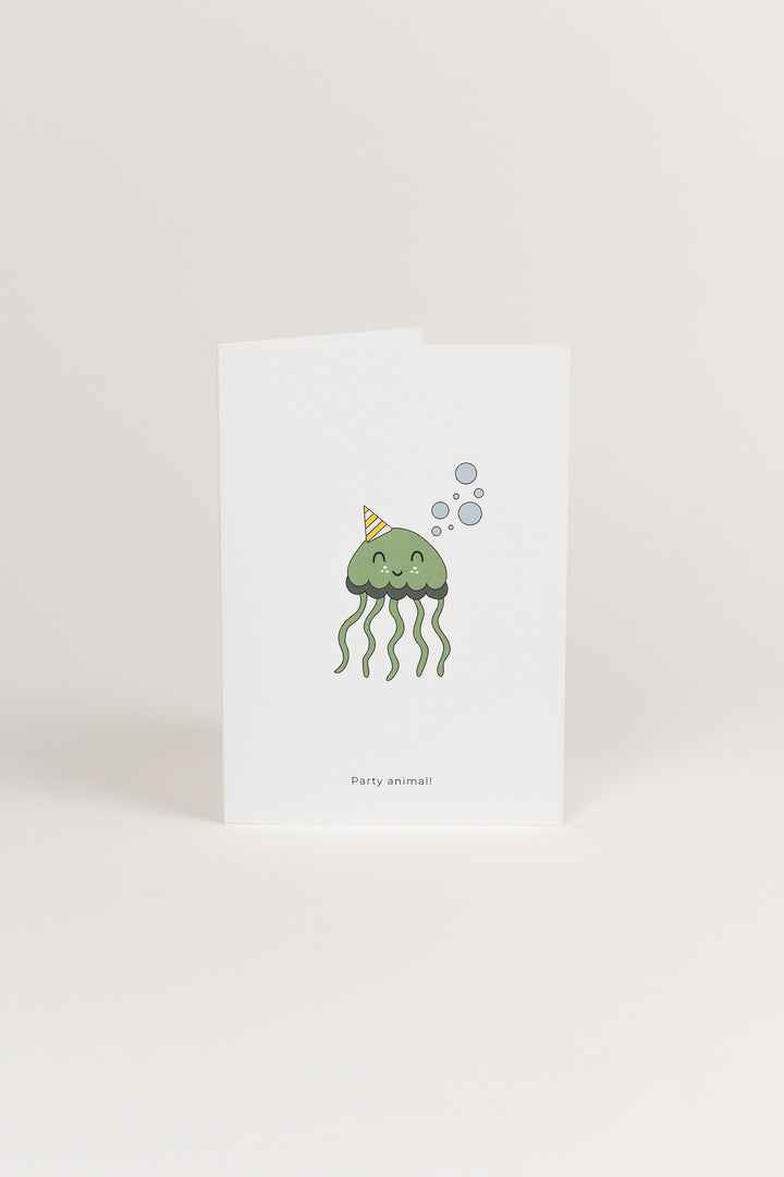 A white Babiem greeting card featuring a cute green jellyfish illustration wearing a striped party hat and surrounded by bubbles. The card has the text “Party animal!” printed below the design.