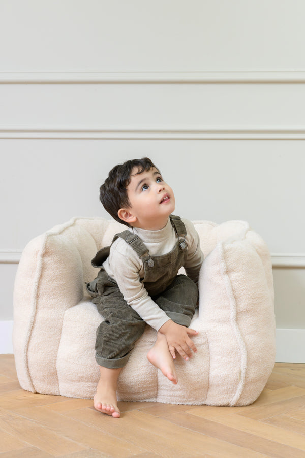 Toddler sitting on the Babiem kids chair Ella in a beige color looking upward while seated on the soft cushioned chair