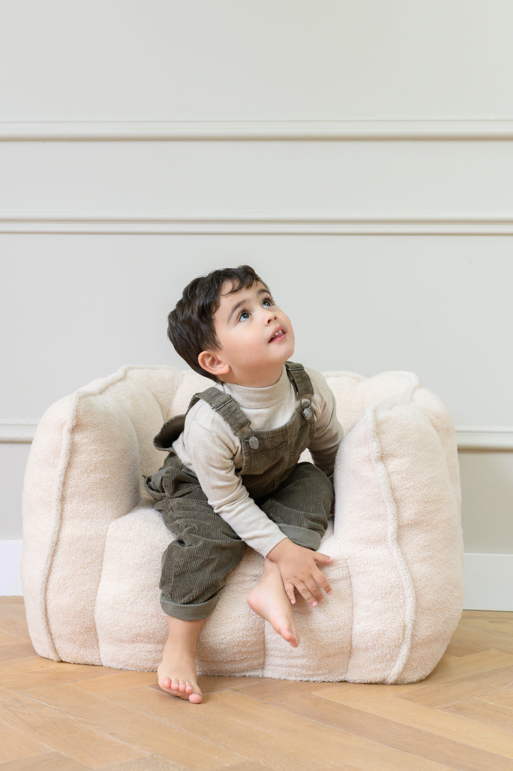 Toddler sitting on the Babiem kids chair Ella in a beige color looking upward while seated on the soft cushioned chair