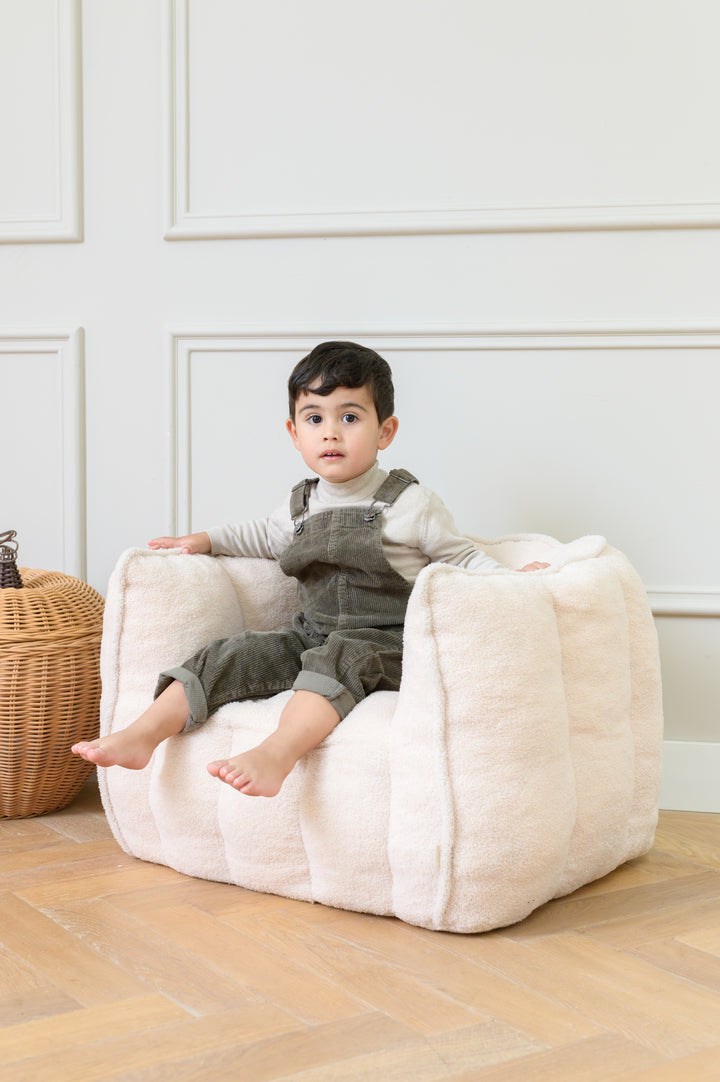 Toddler sitting on the Babiem kids chair Ella in a soft beige fabric looking at the camera with a calm expression
