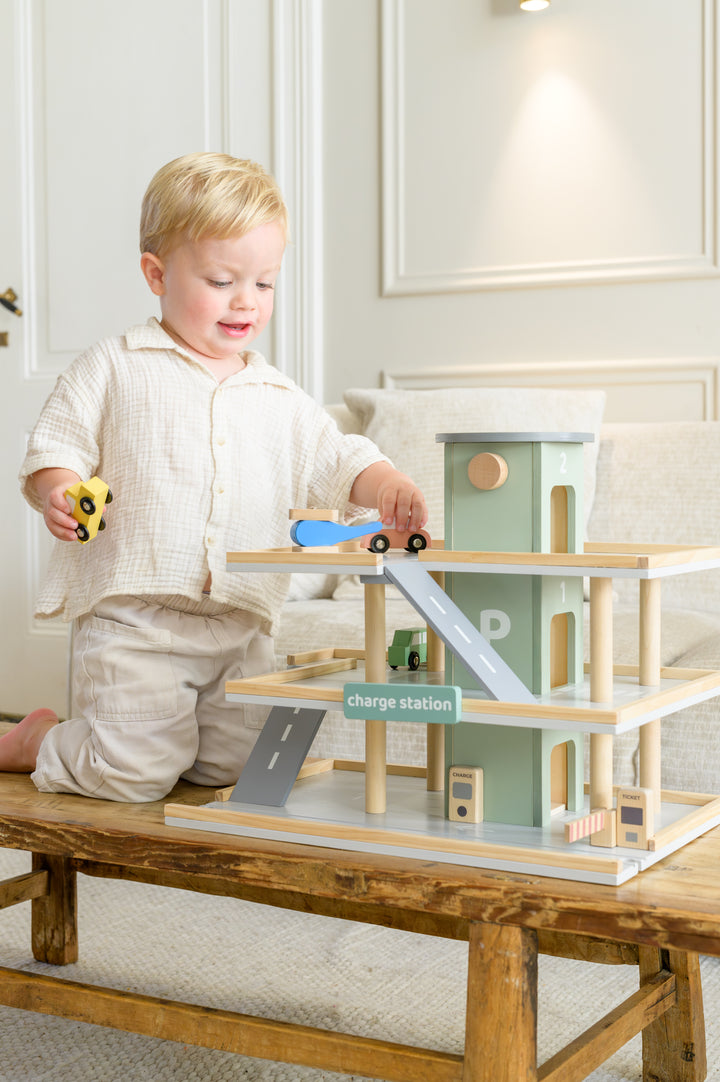 Smiling toddler driving cars and helicopter on the Babiem parking garage Noah wooden play set