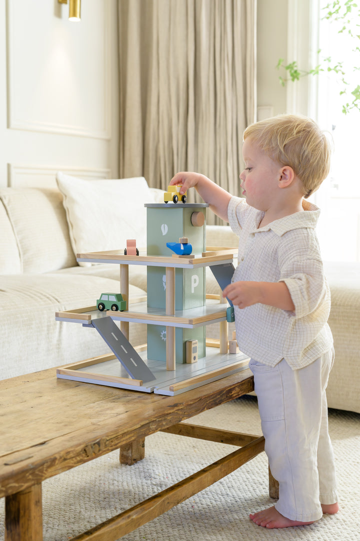 Toddler playing with Babiem parking garage Noah wooden toy set and placing a yellow car on top level