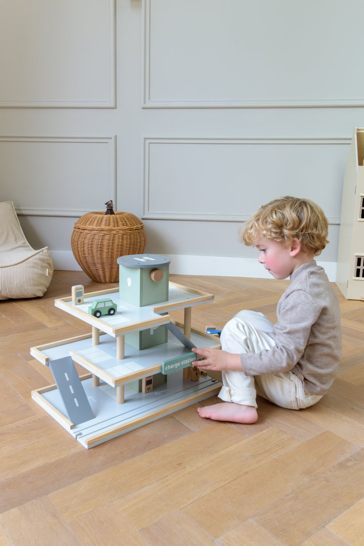 A child playing with the Babiem play garage Noah, moving toy cars around the different parking levels and ramps in a bright, cozy room