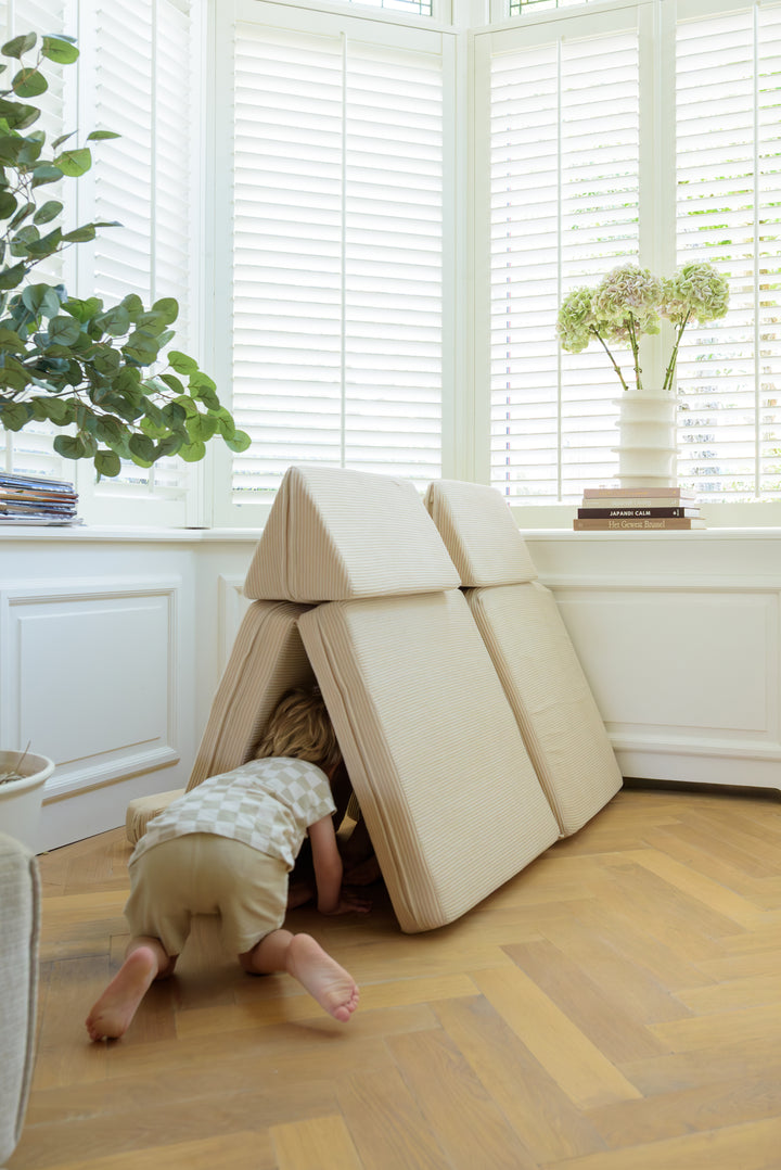 A child crawling into a hut structure made from the 8-piece Babiem play sofa Max, showing how the modular cushions can be creatively arranged for imaginative play.
