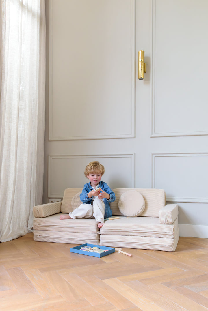 Child sitting on the Babiem play sofa Max in a light filled room with wooden flooring playing with fishing game Emma on a soft beige sofa