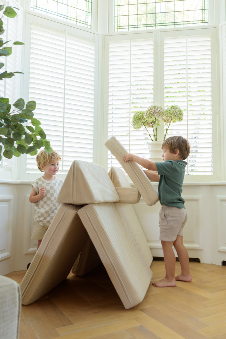 Two children constructing a play structure using the 8-piece Babiem play sofa Max, showing how the modular cushions can be stacked and arranged creatively for imaginative play.
