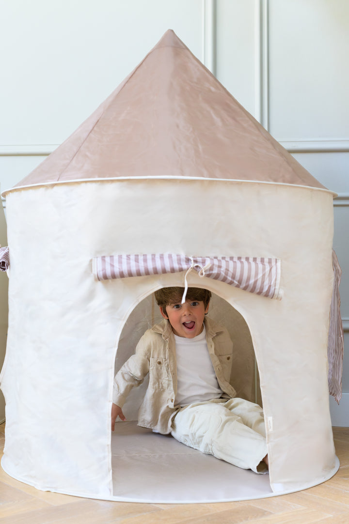 A child sitting and smiling inside the Babiem play tent Alice in a bright room with wooden flooring.