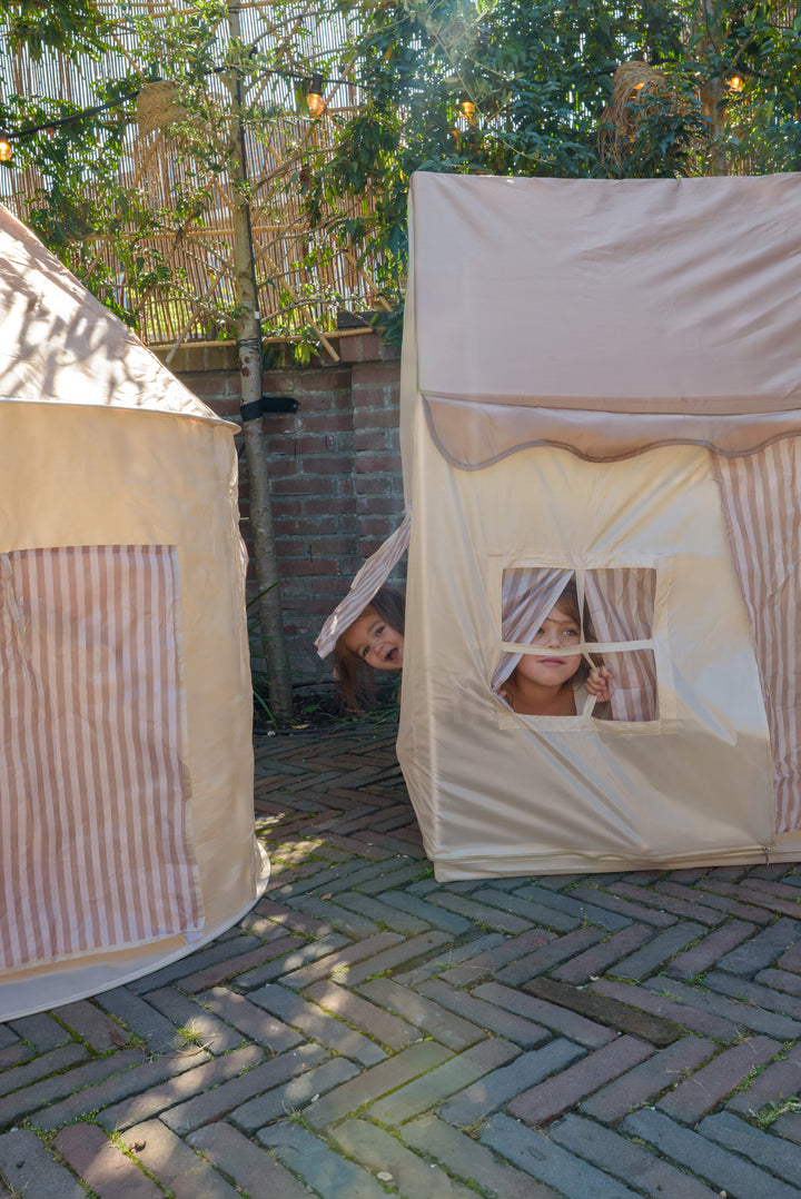 Two children peeking through the striped curtains and window of the Babiem play tent Omar, smiling while playing outside in the garden.