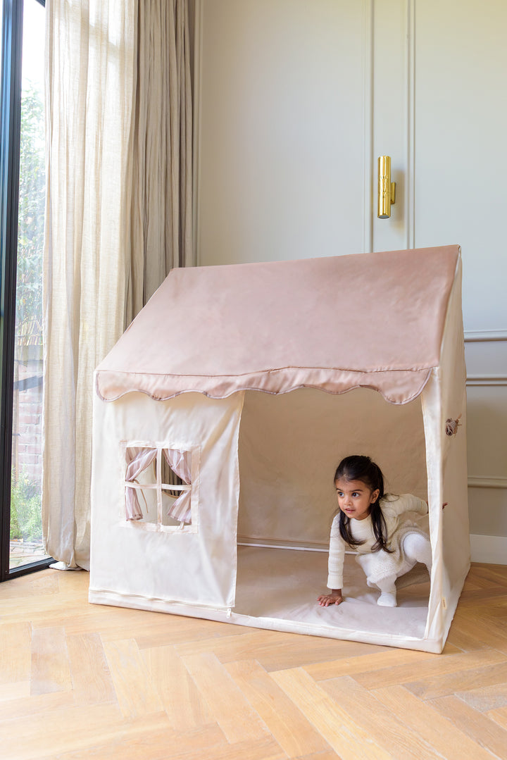 A young girl crawling out of the babiem play tent Omar, set up in a softly lit room with wooden floors and beige curtains