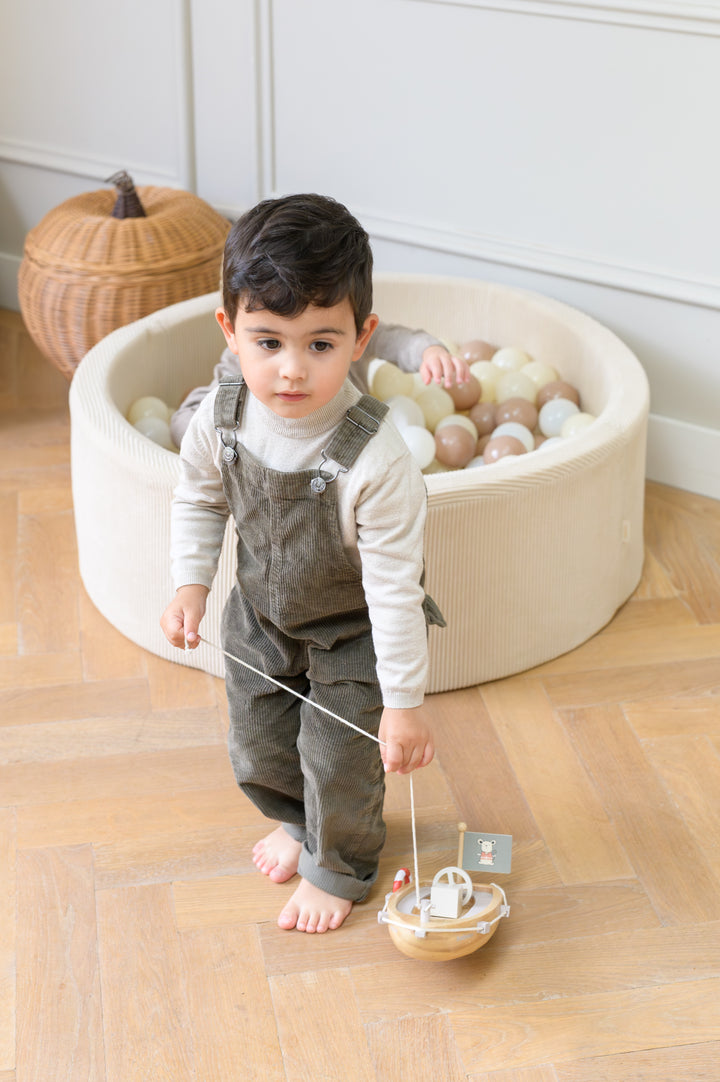 Toddler pulling the Babiem pull-along boat Xavier while standing near a ball pit