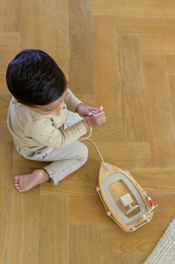 Child sitting on the floor holding the string of the Babiem pull-along boat Xavier