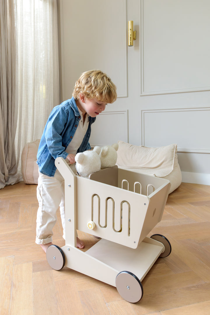 A child pushing the Babiem shopping cart Oliver filled with two stuffed animals in a cozy room.