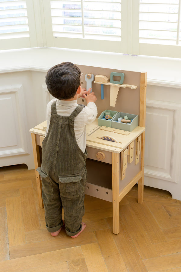 A child standing at the Babiem tool bench Thomas, interacting with the wooden tools and accessories neatly arranged on the pegboard and work surface.