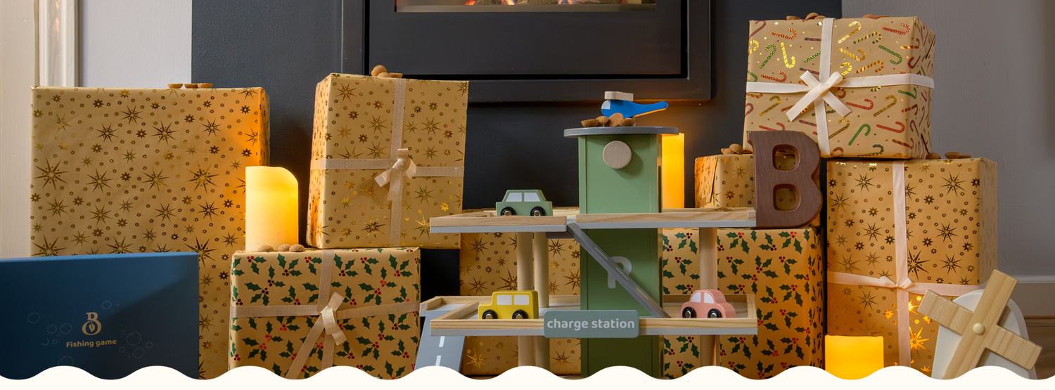A close up of the Babiem play garage Noah surrounded by holiday wrapped presents and glowing candles, showing the wooden garage levels with small toy cars and festive decorations.