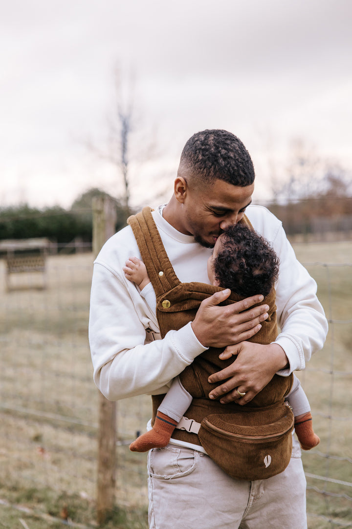 Father lovingly cuddling his baby in the Babiem baby carrier Luca, made of soft brown corduroy with matching fanny pack.