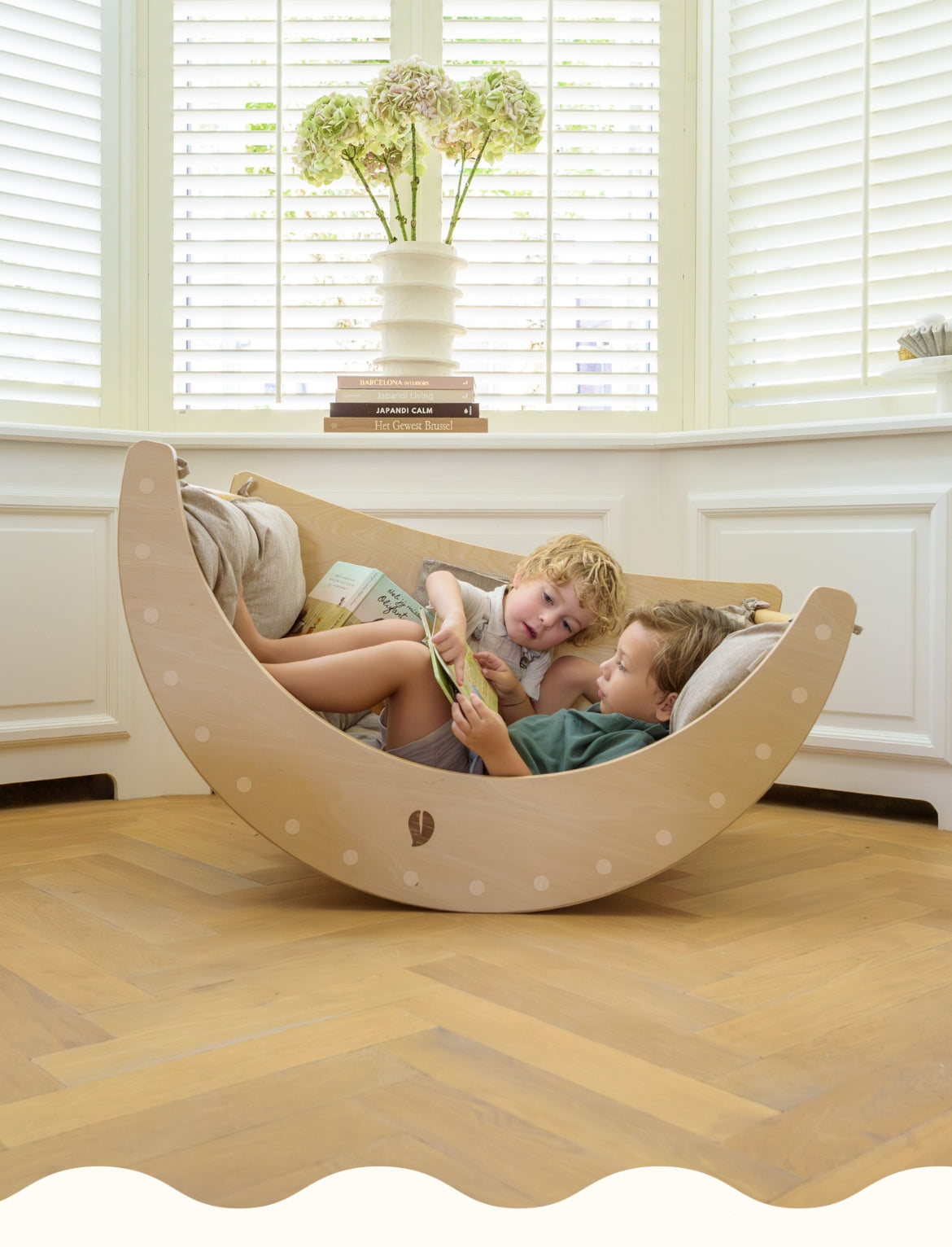 Two childeren relaxing and reading together in the wooden Babiem climbing arch.