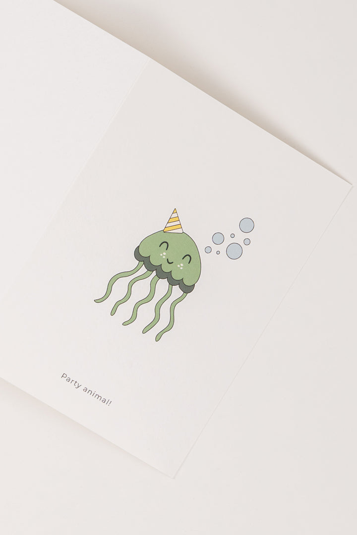 A cute illustrated green jellyfish wearing a striped party hat, surrounded by bubbles, featured on a white Babiem greeting card. The text “Party animal!” is printed below the illustration.