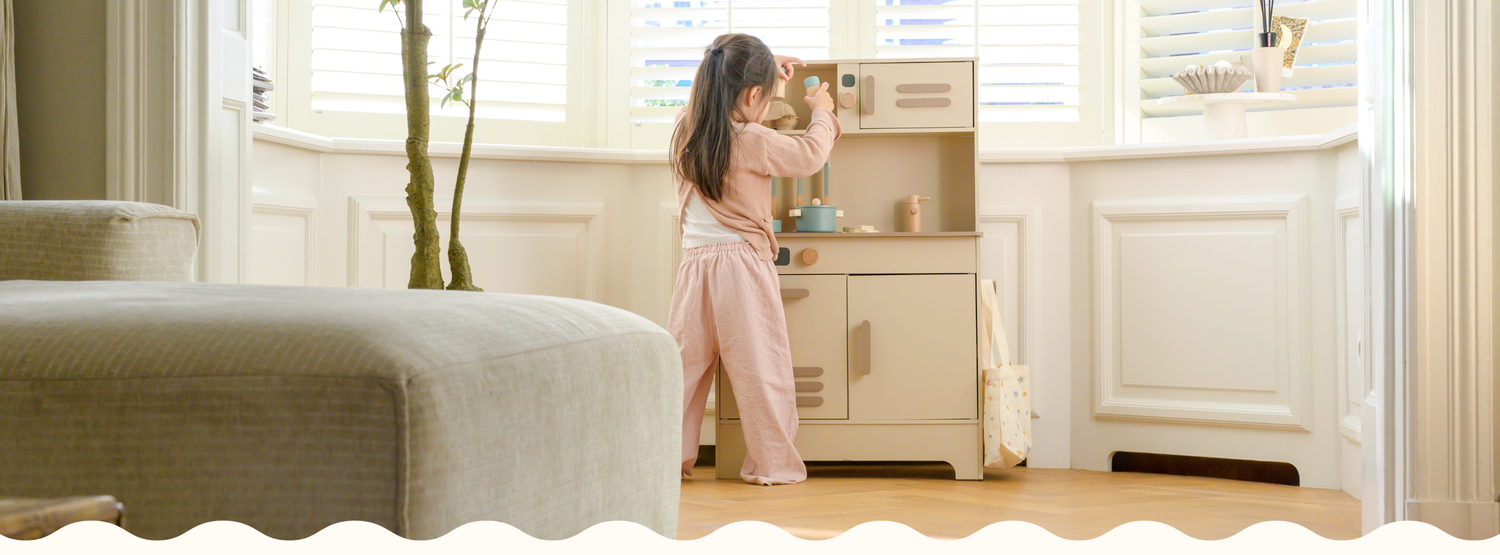 A young girl playing with Babiem’s wooden play kitchen Noor in a bright, cozy room. The soft colors and natural materials reflect Babiem’s commitment to quality, creativity, and durable play.