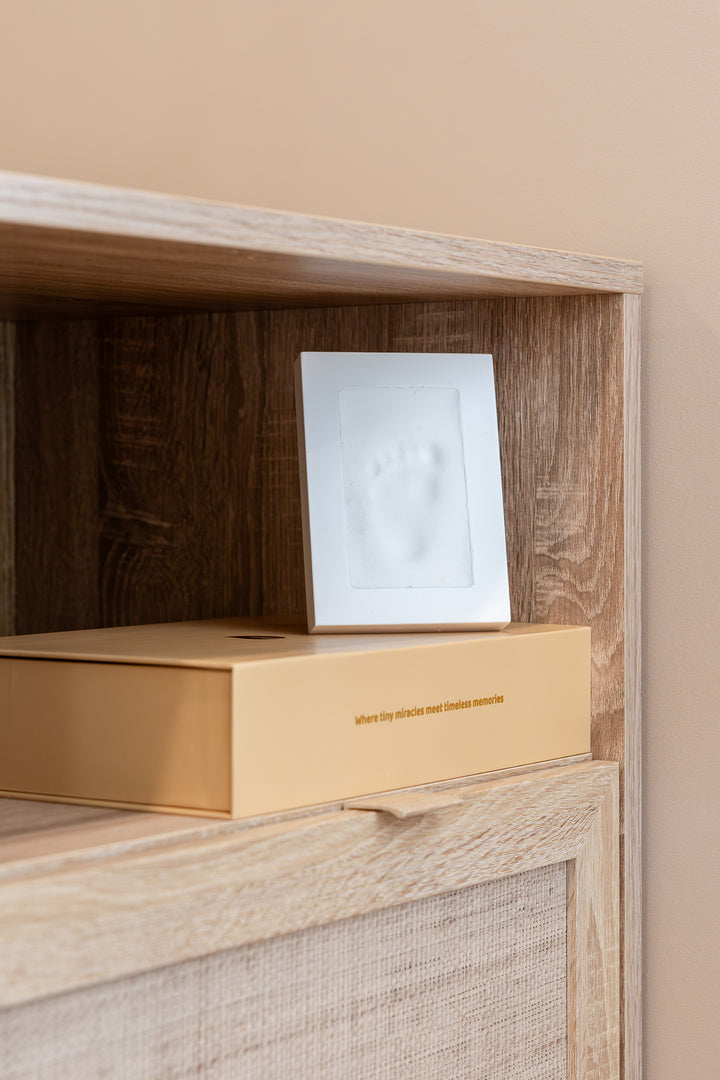 Photo frame from the Babiem memory box featuring a white clay imprint of a baby’s foot, displayed on a beige box with the text “where tiny miracles meet timeless memories”, set on a wooden shelf against a soft beige wall.