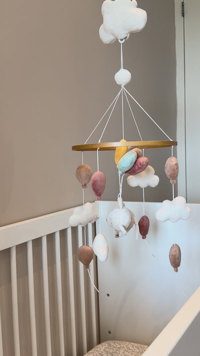 The Babiem music mobile Sam hanging above a baby’s crib, featuring a soft plush mouse floating among pastel-colored balloons and fluffy clouds. The gentle motion and soothing music create a dreamy, comforting atmosphere for the nursery.