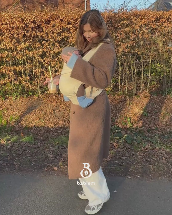 A mother carrying her baby in the Olivia baby carrier of Babiem on a autumn day in earthy colours.