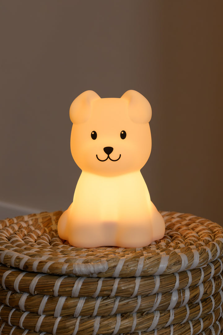 Close-up of the Babiem Bibi night lamp in the shape of a bear, shining a warm amber light in a calm and natural setting.